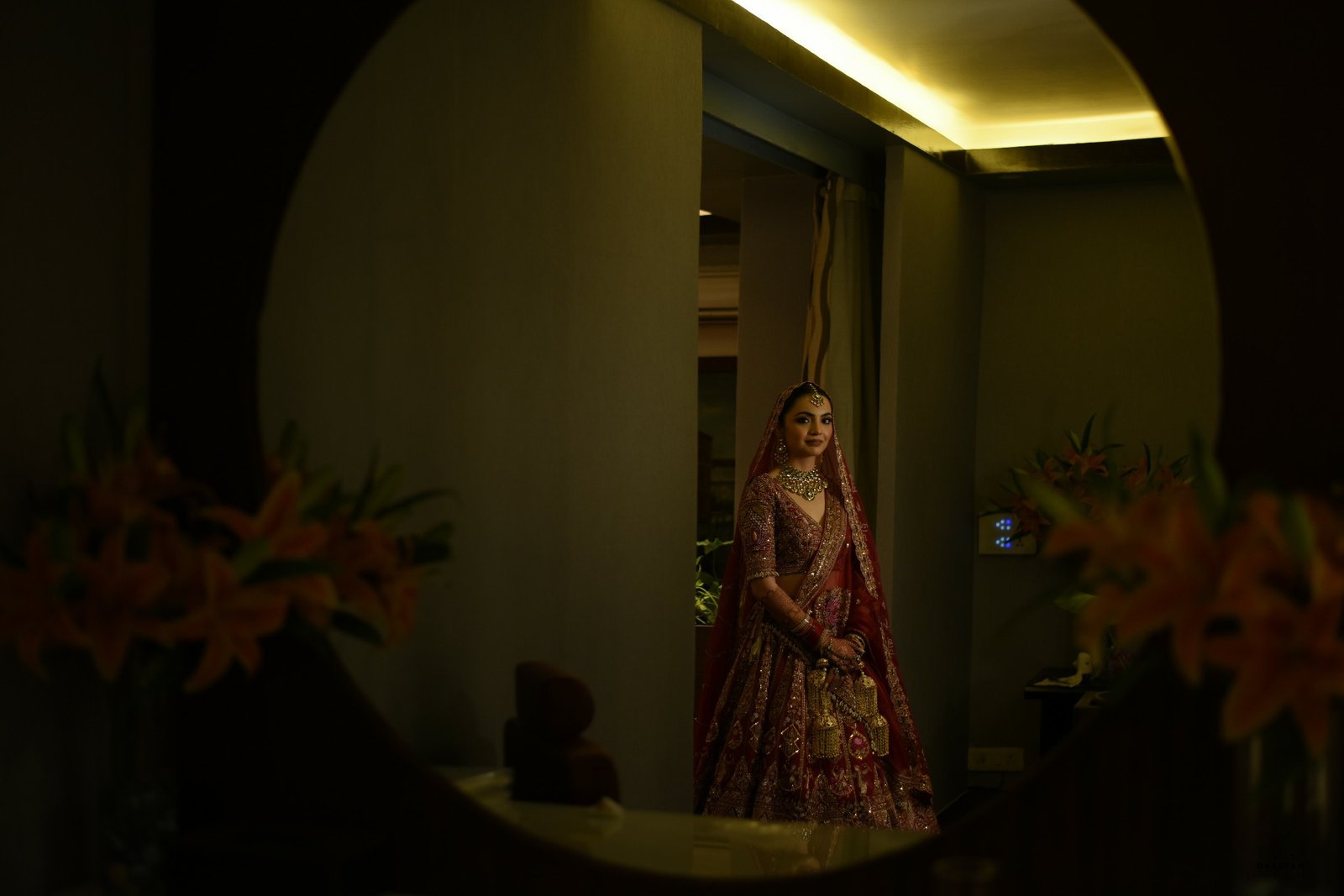 Full portrait of bride in bridal lehenga with lush floral decor background at Indian wedding reception