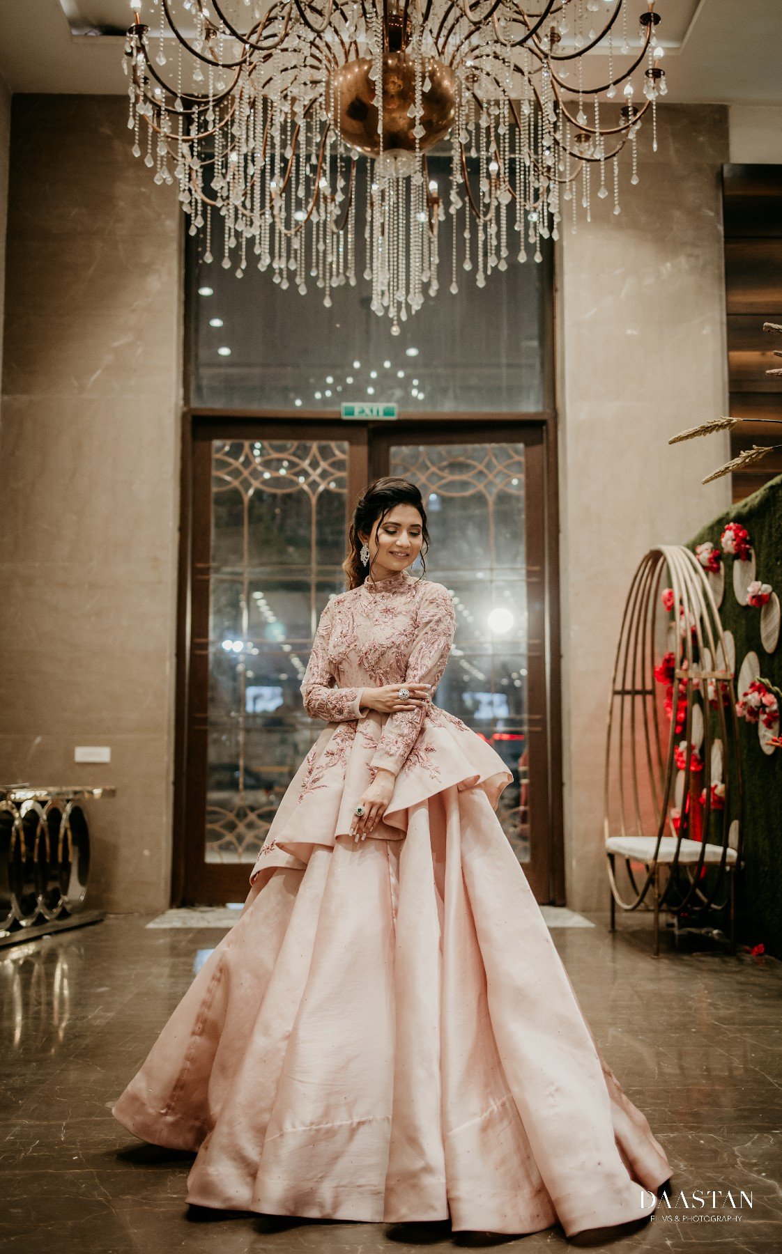 Bride in blush pink lehenga with grand chandelier backdrop, luxury reception wedding photography India
