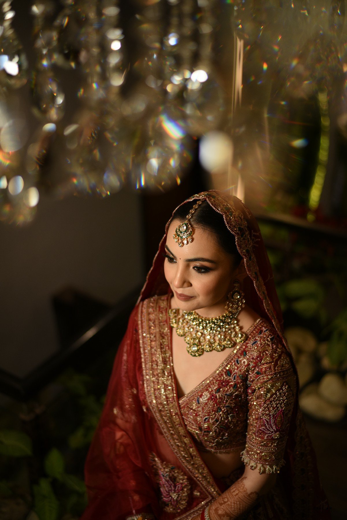 Cinematic portrait of bride in deep red lehenga under chandelier, editorial wedding photography India