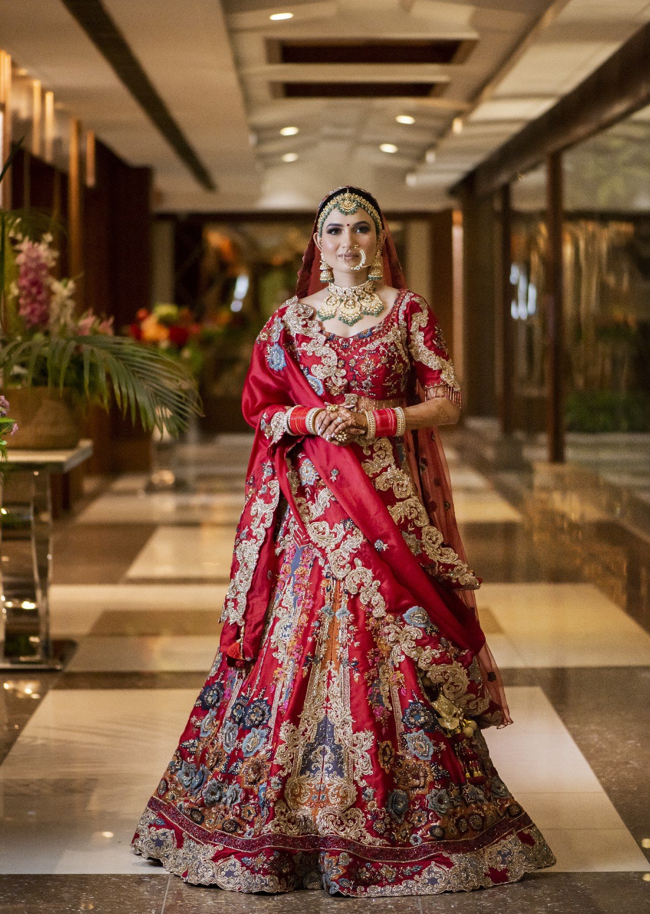 Full-length portrait of bride in vibrant red embroidered lehenga in hotel lobby, Indian wedding photography