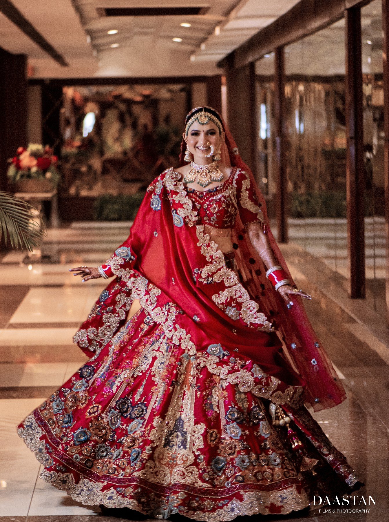 Bride in stunning red bridal lehenga walking through luxury hotel reception, cinematic wedding photography