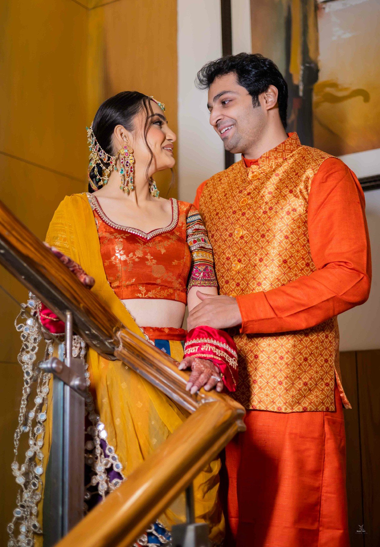 Couple in yellow haldi outfits posing on staircase, pre-wedding portrait Indian wedding production house