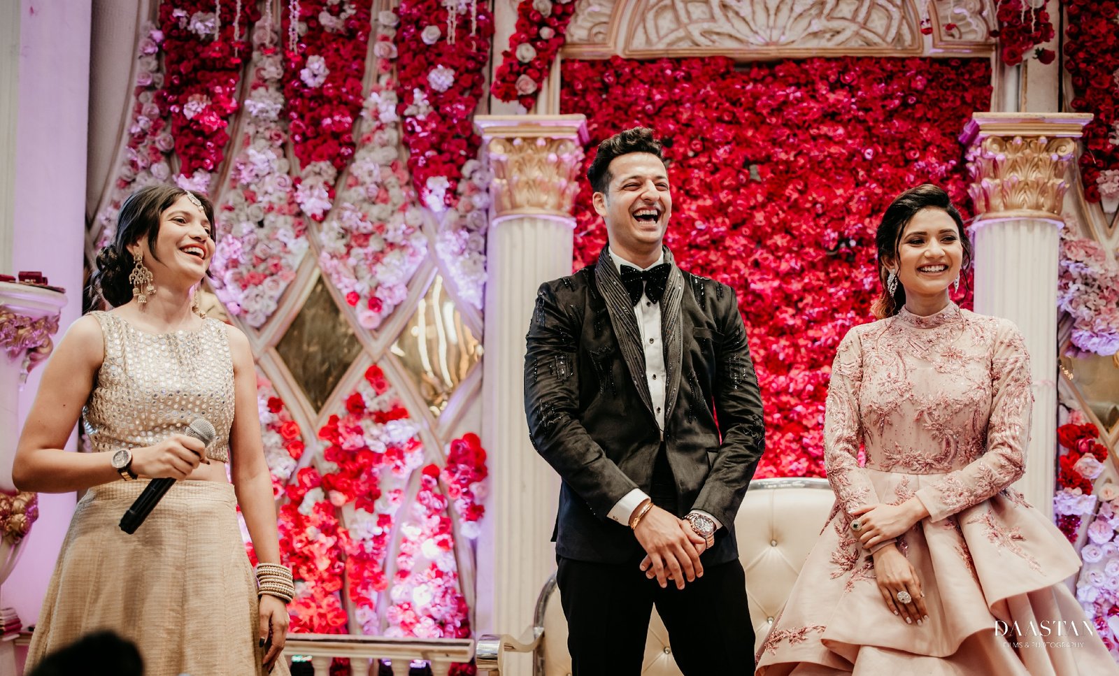 Bride and groom on wedding stage with rose wall floral backdrop, luxury Indian wedding photography
