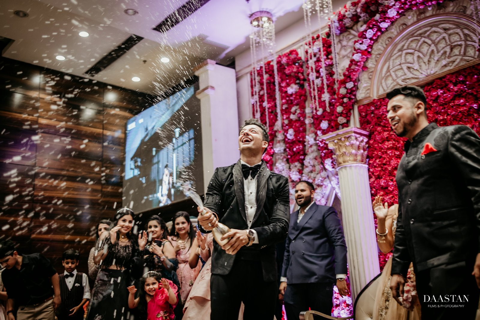 Groom tossing rose petals in celebration at reception, joyful candid Indian wedding photography