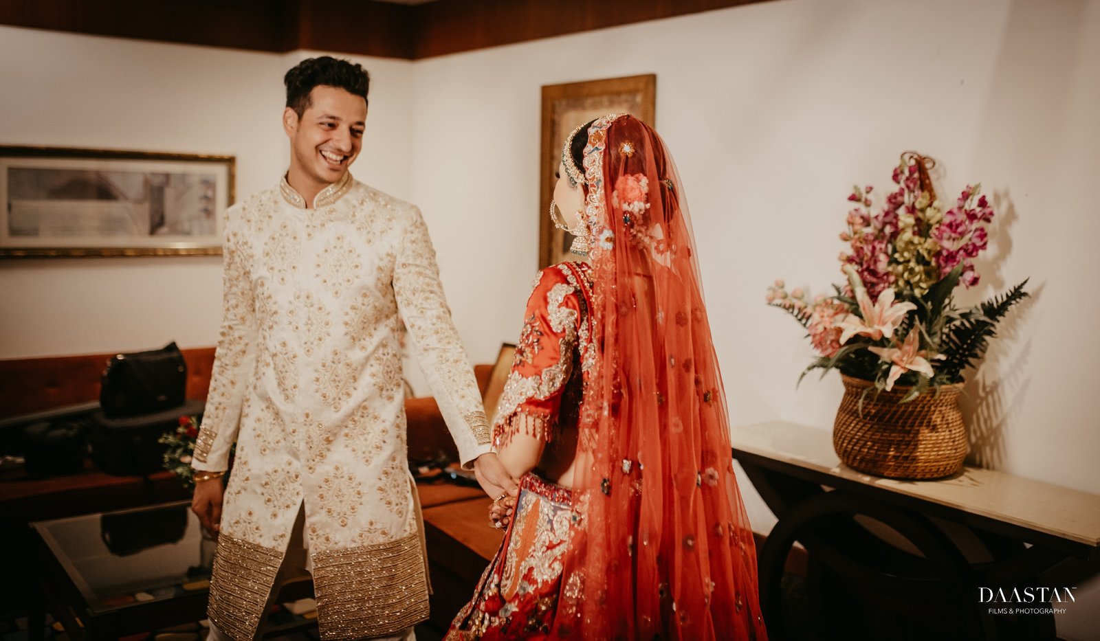 Stunning Indian bride in red lehenga standing with groom in luxury hotel, professional wedding photography